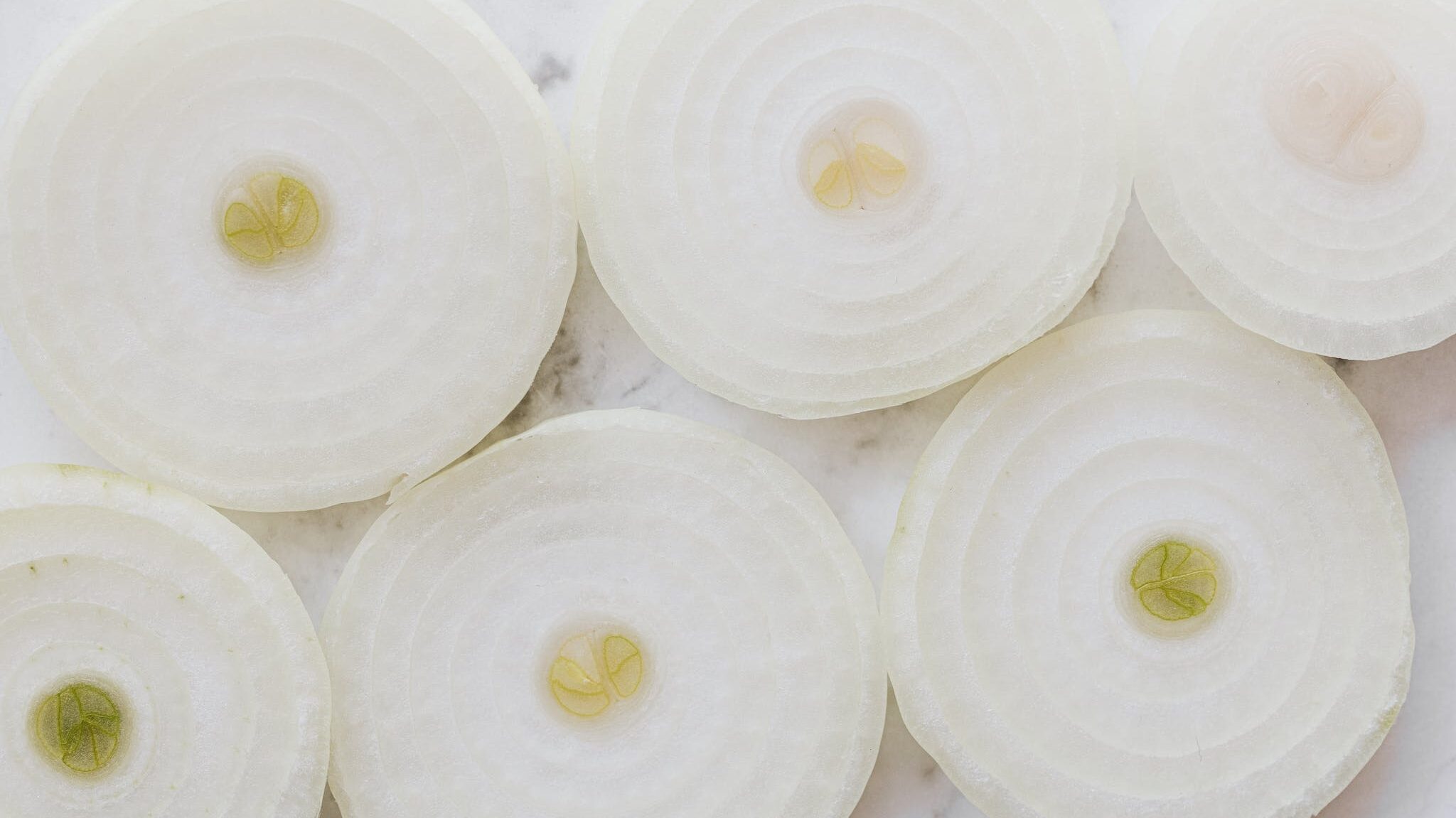 Top view closeup of ripe organic yellow peeled onion cut into rings and placed on white marble tabletop
